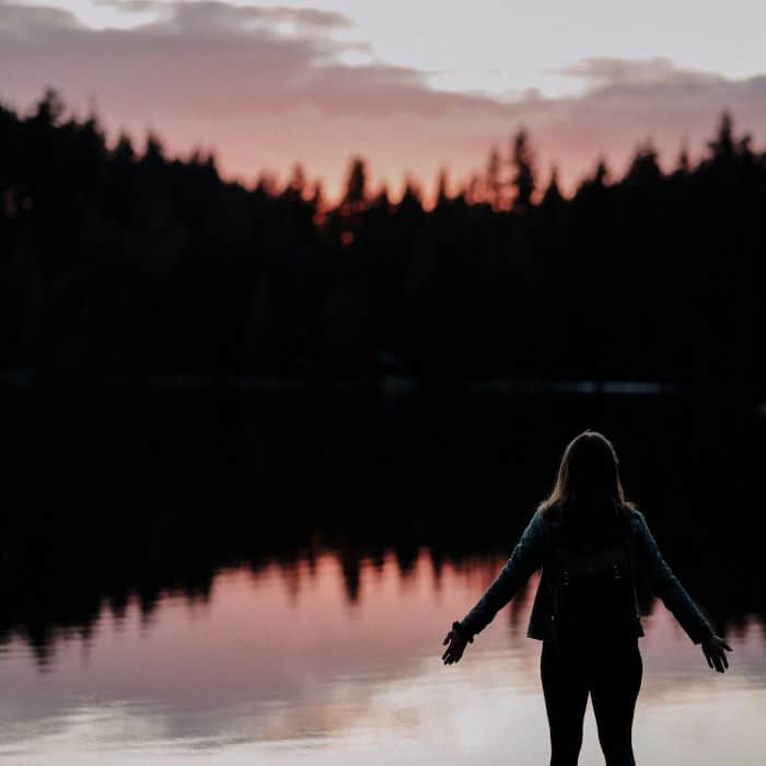 woman standing in front of lake with arms open